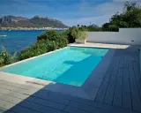Piscina cristallina con vista mare. L'acqua, mantenuta con candeggina a un ph ideale, riflette il cielo azzurro e le montagne sullo sfondo.