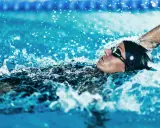 Atleta in nuoto dorso, godendo dei benefici di questo sport. L'acqua schizza intorno al suo viso concentrato.
