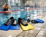 Pinne corte blu e gialle, occhialini e cuffia da piscina pronti per un allenamento.