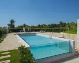 Piscina fuori terra su terreno in pendenza con pareti in vetro, circondata da un giardino curato e un'area relax con lettini e gazebo.
