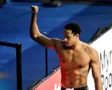 Shane Tusup, nuotatore con un pugno alzato, celebra una vittoria. Sul suo petto, i cinque cerchi olimpici.