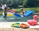 Bambini si divertono in piscina con gonfiabili colorati, tra cui un unicorno e un fenicottero. Perfetti giochi da fare in piscina senza niente per un'estate indimenticabile.