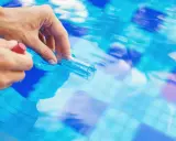 Mano che preleva campione d'acqua piscina con provetta. Il cloro basso indica necessità di trattamento.