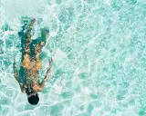 Persona sott'acqua in piscina, con riflessi luminosi. Chissà se il suo tatuaggio è fresco, dopo quanto tempo in piscina?