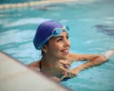 Donna sorridente in piscina con cuffia e occhialini, pronta a scoprire quante vasche in un'ora.