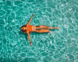 Donna rilassata galleggia in piscina. Il nuoto è un ottimo modo per migliorare la forma fisica, con risultati visibili nel nuoto cellulite prima e dopo.