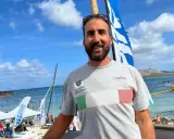 Fabrizio Antonelli sorride in spiaggia, con la bandiera italiana sul petto, pronto per un evento di nuoto.