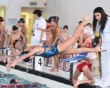 Axana Merckx, giovane nuotatrice, si tuffa in piscina con agilità. Allenatrice osserva la gara.