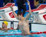 Nuotatore con braccia alzate, festeggia la vittoria. Pan Zhanle trionfa in piscina, circondato da avversari e blocchi di partenza.
