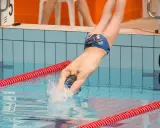 Un atleta si tuffa in piscina, mostrando la sua massa muscolare sviluppata grazie al nuoto. L'acqua schizza mentre entra in azione.