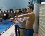 Nuotatore pronto a gareggiare, forse Matt Grevers, con allenatori al bordo piscina.