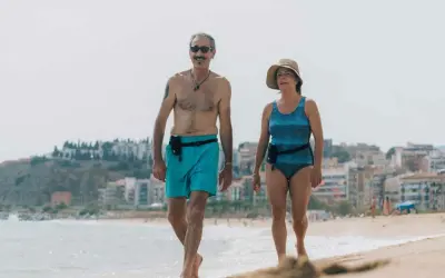 Coppia over 60 passeggia sulla spiaggia, un esempio di allenamento nuoto e vita attiva.