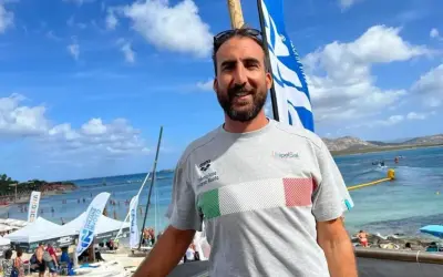 Fabrizio Antonelli sorride in spiaggia, con la bandiera italiana sul petto, pronto per un evento di nuoto.