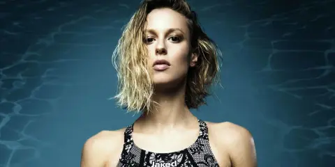 Francesca Pellegrini, nuotatrice con capelli bagnati e costume Jaked, posa con sguardo intenso su sfondo blu con riflessi d'acqua.