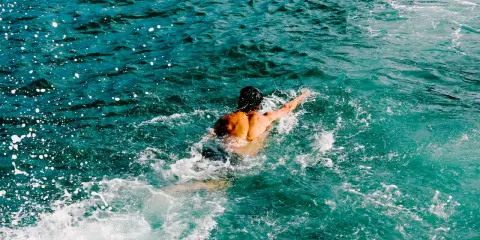 Uomo con schiena muscolosa nuotare in mare aperto, circondato da spruzzi d'acqua cristallina.