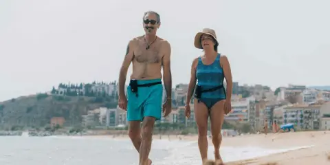 Coppia over 60 passeggia sulla spiaggia, un esempio di allenamento nuoto e vita attiva.