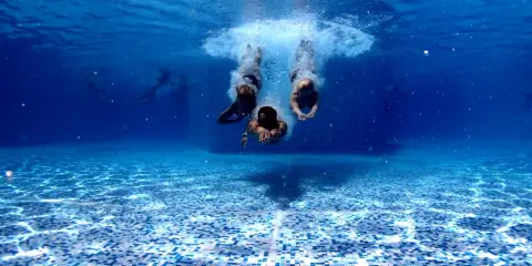 Subacquea, tre persone si tuffano in piscina. Chissà in quanto tempo un adulto impara a nuotare, ma loro sembrano già a loro agio.