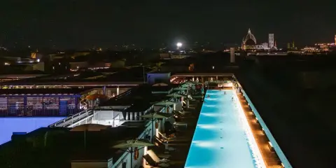 Una splendida piscina di sera, illuminata da luci soffuse, con la silhouette di Firenze sullo sfondo.