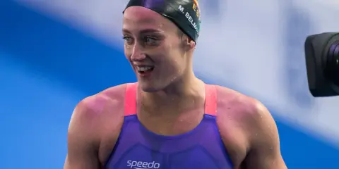 Mireia Belmonte, bagnata e sorridente, indossa un costume da nuoto viola e una cuffia nera.