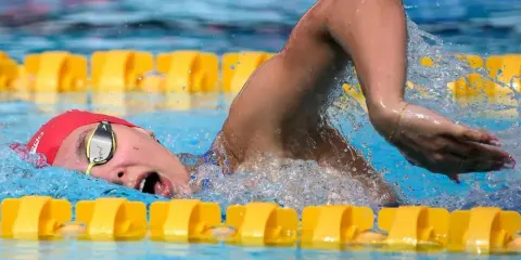 Nuotatrice con cuffia rossa e occhialini, in azione in piscina. Camille Muffat, un'atleta determinata.