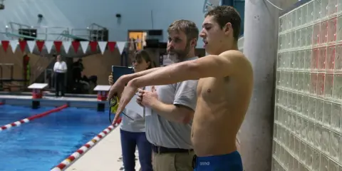 Nuotatore pronto a gareggiare, forse Matt Grevers, con allenatori al bordo piscina.
