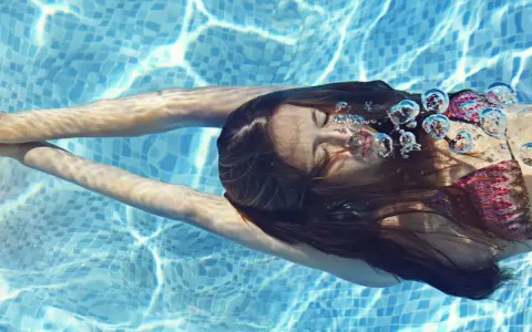 Ragazza nuota sott'acqua, capelli scuri fluttuano. Le bollicine d'aria evidenziano gli effetti del cloro sui capelli.