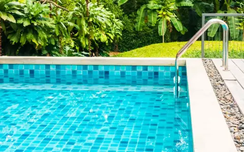 Piscina fuori terra con piastrelle blu scintillanti e vegetazione lussureggiante. La manutenzione piscina fuori terra è fondamentale per godersi questo angolo di paradiso.