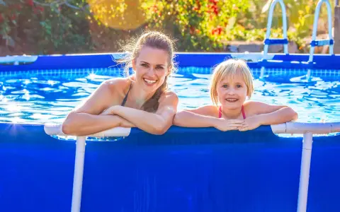 Donna e bambina sorridono in piscina. L'acqua limpida, forse trattata con bicarbonato, riflette il sole.