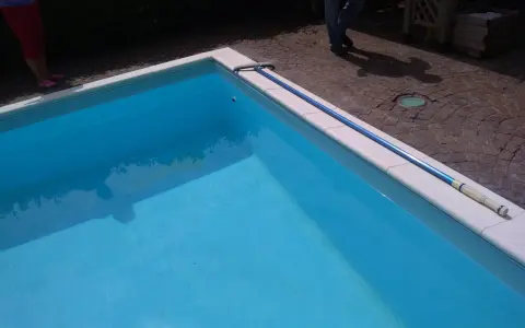 Piscina bucata: un'asta telescopica blu giace sul bordo bianco, pronta per cercare il buco.