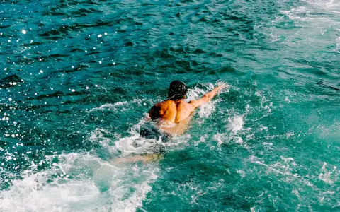 Uomo con schiena muscolosa nuotare in mare aperto, circondato da spruzzi d'acqua cristallina.