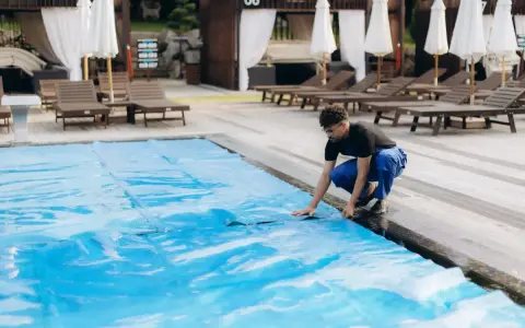 Uomo in blu sistema il telo in pvc della piscina, un passo fondamentale per capire come pulire il telo in pvc della piscina e mantenerla splendente.