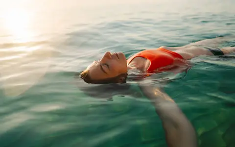 Donna galleggia serena in acqua cristallina, pensando ai rimedi per l'otite del nuotatore.