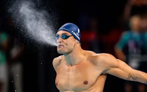 Florent Manaudou, nuotatore francese, spruzza acqua dalla bocca dopo una gara, con la cuffia blu e gli occhialini da nuoto.