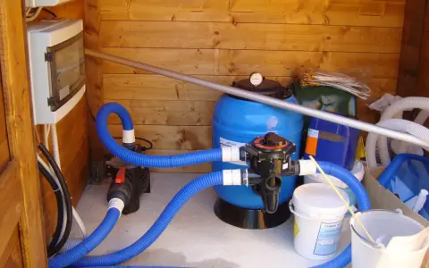 Sistema di filtrazione per piscina con filtro a sabbia, pompa e tubi blu. Il filtro a sabbia è il cuore del sistema per mantenere l'acqua pulita.
