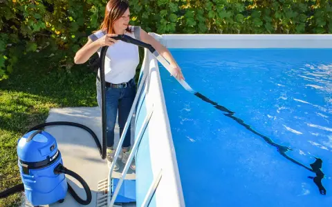 Donna pulisce la piscina con un aspiratore, preparandola per la riapertura dopo l'inverno.