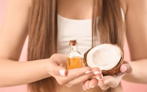 Mani che tengono una boccetta di olio di cocco e mezzo cocco. Ideale per proteggere i capelli dopo la piscina.