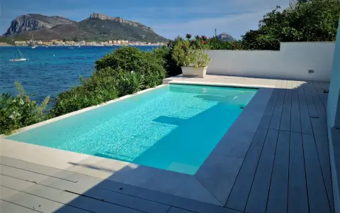 Piscina cristallina con vista mare. L'acqua, mantenuta con candeggina a un ph ideale, riflette il cielo azzurro e le montagne sullo sfondo.