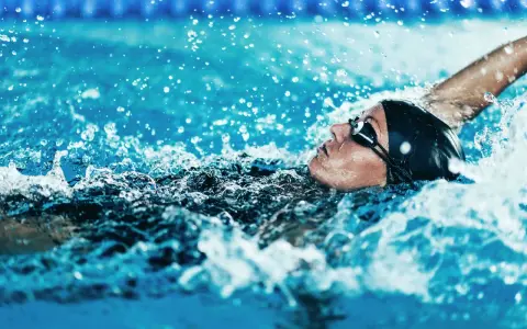 Atleta in nuoto dorso, godendo dei benefici di questo sport. L'acqua schizza intorno al suo viso concentrato.