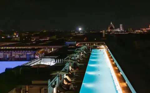 Una splendida piscina di sera, illuminata da luci soffuse, con la silhouette di Firenze sullo sfondo.