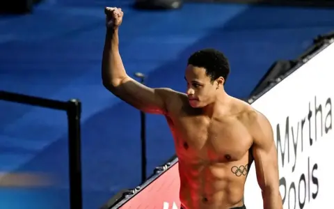 Shane Tusup, nuotatore con un pugno alzato, celebra una vittoria. Sul suo petto, i cinque cerchi olimpici.