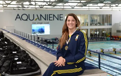Rachele Ceracchi, nuotatrice sorridente con medaglia al collo, posa in un centro sportivo con piscina.