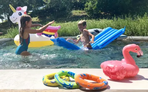 Bambini si divertono in piscina con gonfiabili colorati, tra cui un unicorno e un fenicottero. Perfetti giochi da fare in piscina senza niente per un'estate indimenticabile.