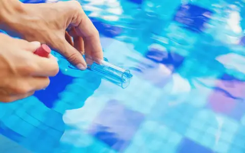 Mano che preleva campione d'acqua piscina con provetta. Il cloro basso indica necessità di trattamento.