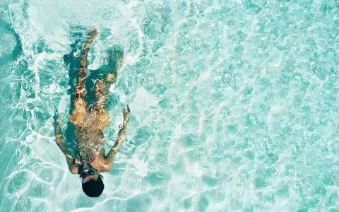 Persona sott'acqua in piscina, con riflessi luminosi. Chissà se il suo tatuaggio è fresco, dopo quanto tempo in piscina?