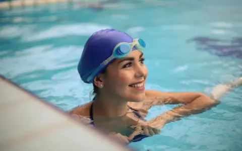 Donna sorridente in piscina con cuffia e occhialini, pronta a scoprire quante vasche in un'ora.
