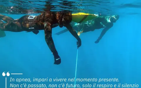 Due apneisti nuotano sott'acqua, uno vicino alla superficie. Imparare a trattenere il respiro, come rompere il fiato, porta a vivere il momento presente.