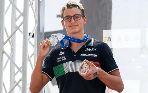 Davide Grossi, nuotatore italiano, mostra con orgoglio le sue medaglie d'argento e di bronzo, frutto di un'ottima prestazione.