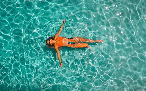 Donna rilassata galleggia in piscina. Il nuoto è un ottimo modo per migliorare la forma fisica, con risultati visibili nel nuoto cellulite prima e dopo.