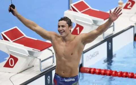 Il nuotatore Nicolò Martinenghi, con il suo fisico scolpito, esulta con le braccia alzate dopo una gara.