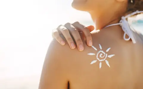 Sole sulla pelle, ma attenzione: il cloro toglie l'abbronzatura. Crema solare a forma di sole sulla spalla di una donna in spiaggia.